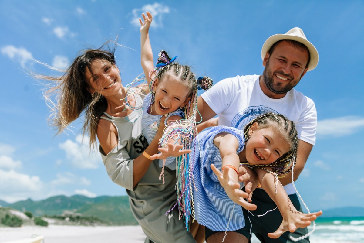 Família com duas crianças brincando na praia em um dia de sol
