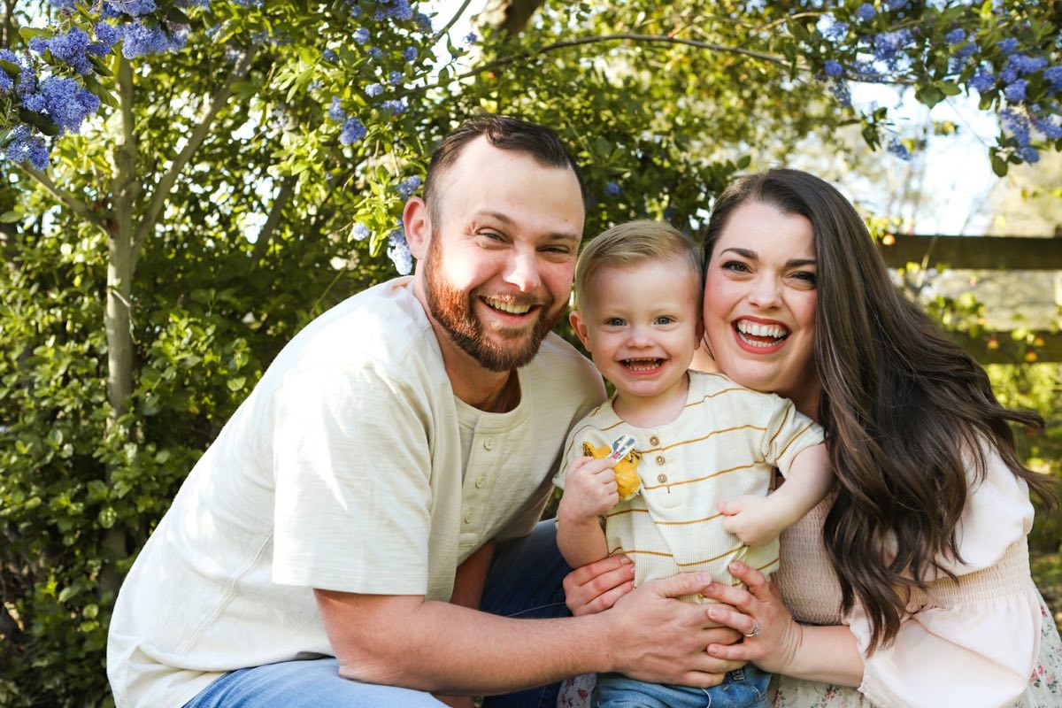 Casal sorrindo com o bebê no colo, ao ar livre